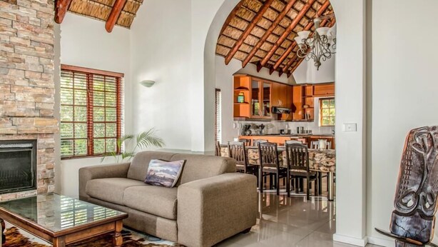 A living room with a sofa, TV, and coffee table, a fireplace, and a kitchen visible through an archway. - St Francis Bay Luxury Lodge 2 (Saint Francis Bay)