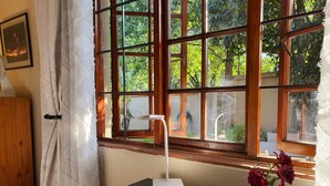 A room with a large window, a desk with a remote control, a lamp, and a vase with flowers. - Pepper Tree BnB (Sandton)