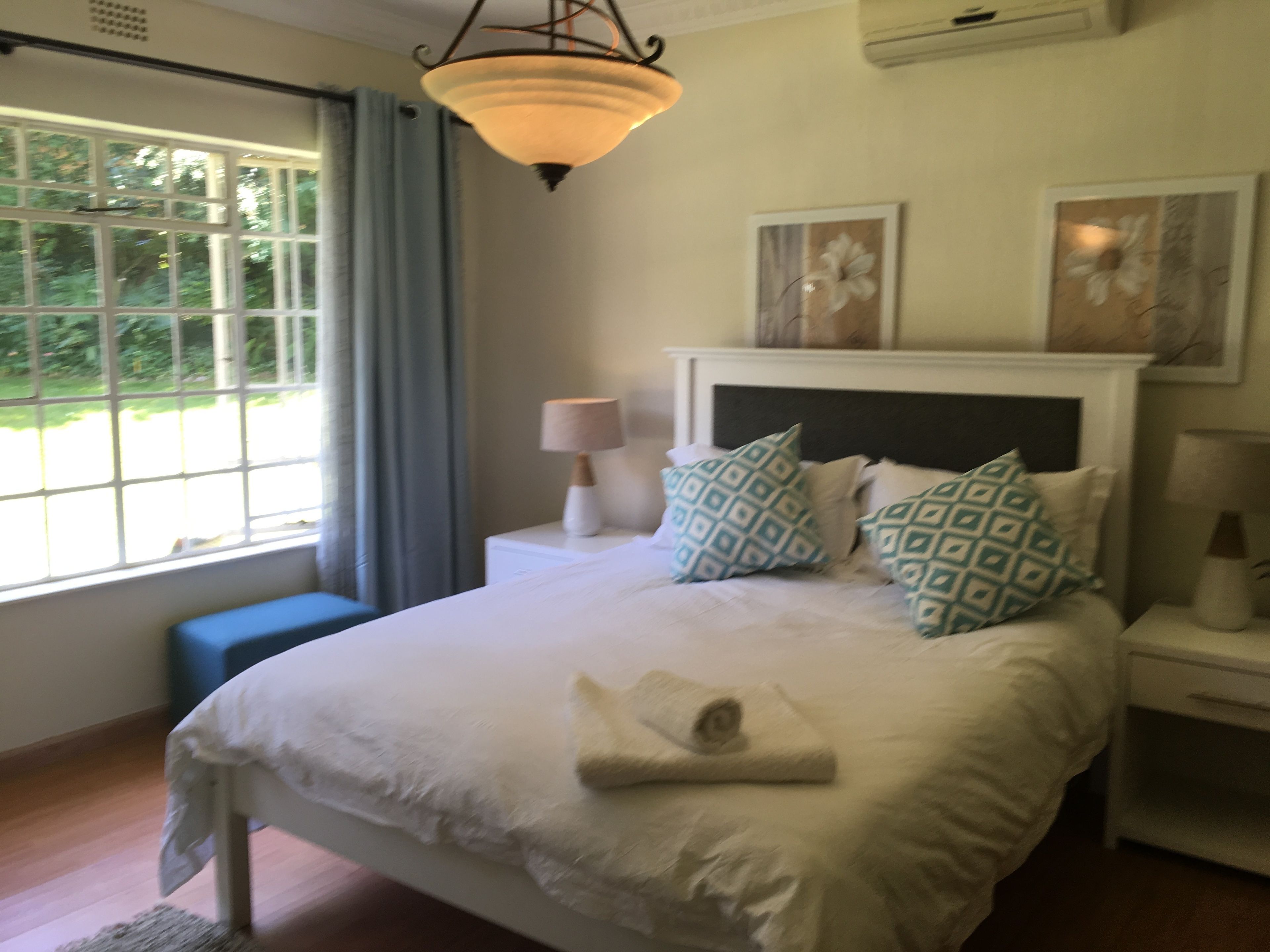 Quarto com cama, mesa de cabeceira, luminária, janela com cortinas e ar-condicionado fixado na parede.
