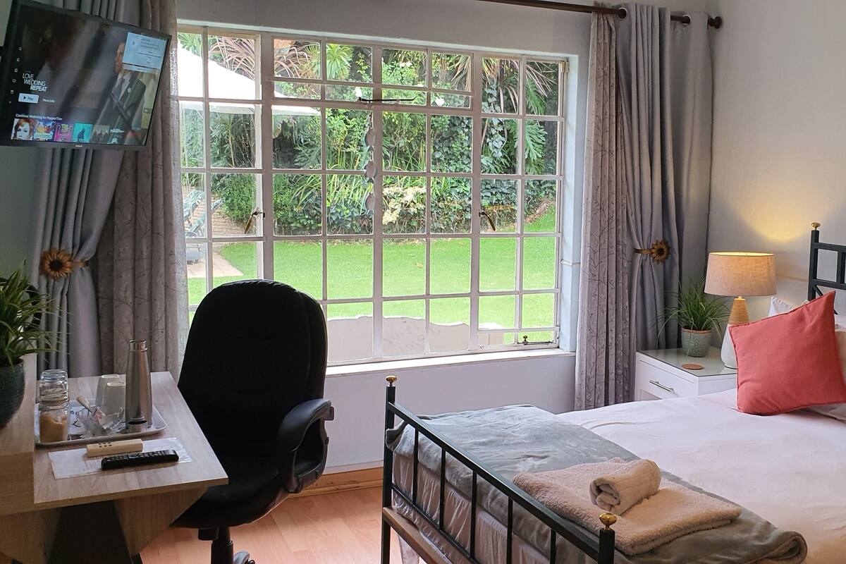 A hotel room with a bed, a desk with a chair, a TV, and a window with curtains.