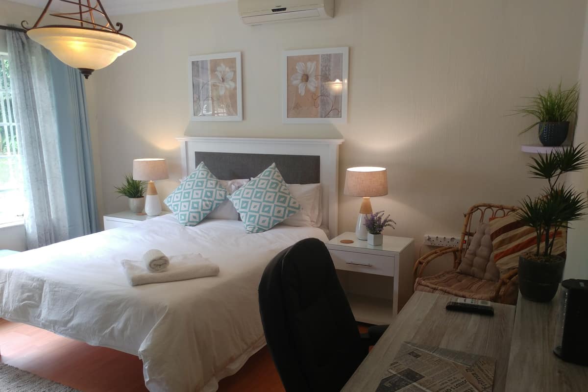 A hotel room with a bed, two nightstands, a chair, a table with newspapers, and a window with curtains.