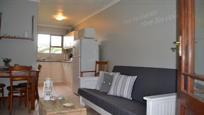 A compact living space with a sofa, dining table, chairs, and a kitchenette. - African Sun Guest House (George)