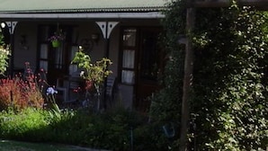 A building with a covered porch, hanging flower baskets, and a well-maintained garden. - African Sun Guest House (George)