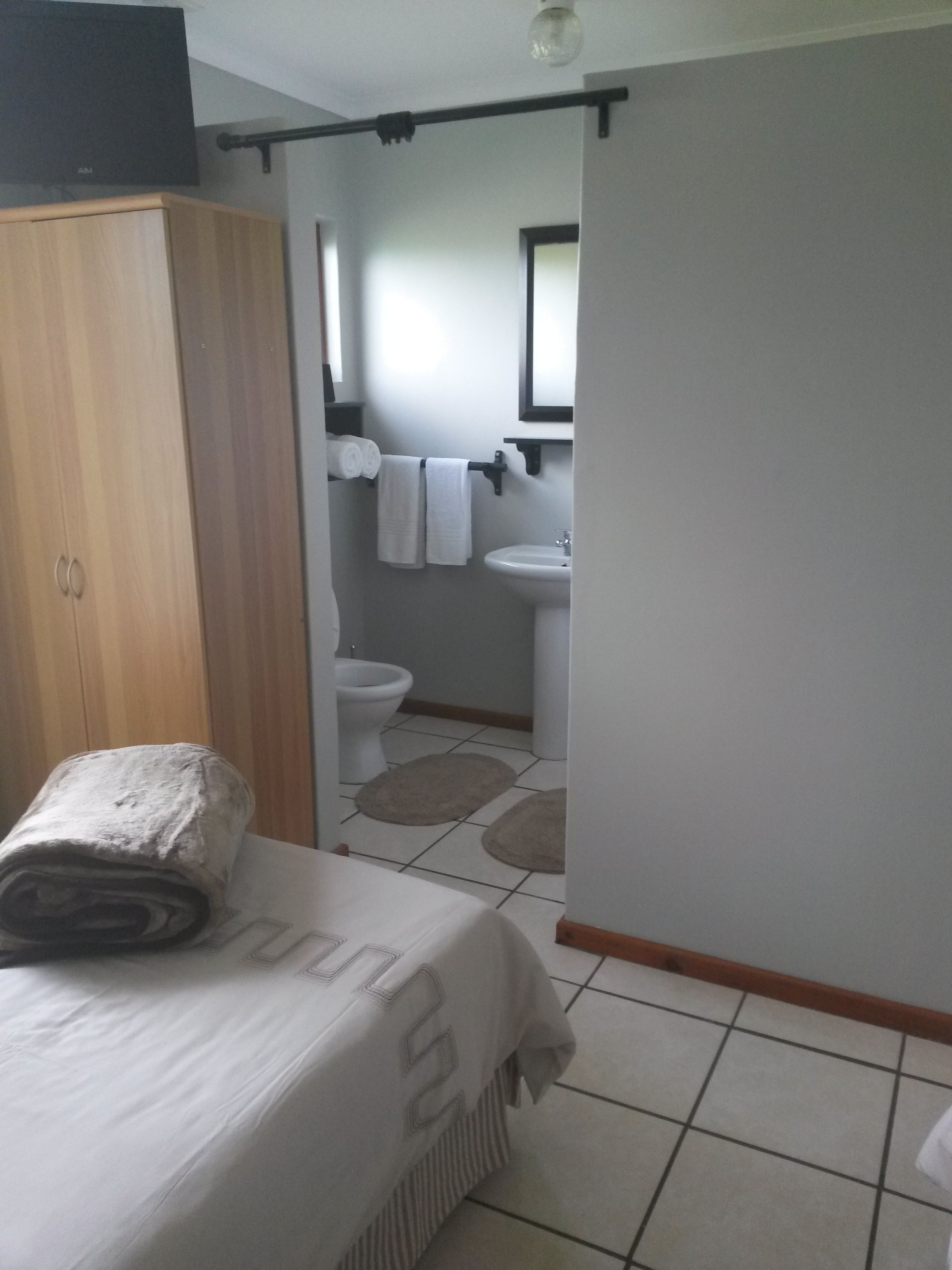 Quarto com cama, guarda-roupa e vista para um banheiro com vaso sanitário, pia e toalhas.