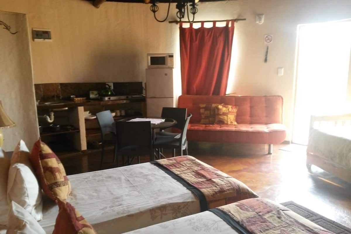 A room with two beds, a dining table with chairs, a kitchen area, and a red sofa.