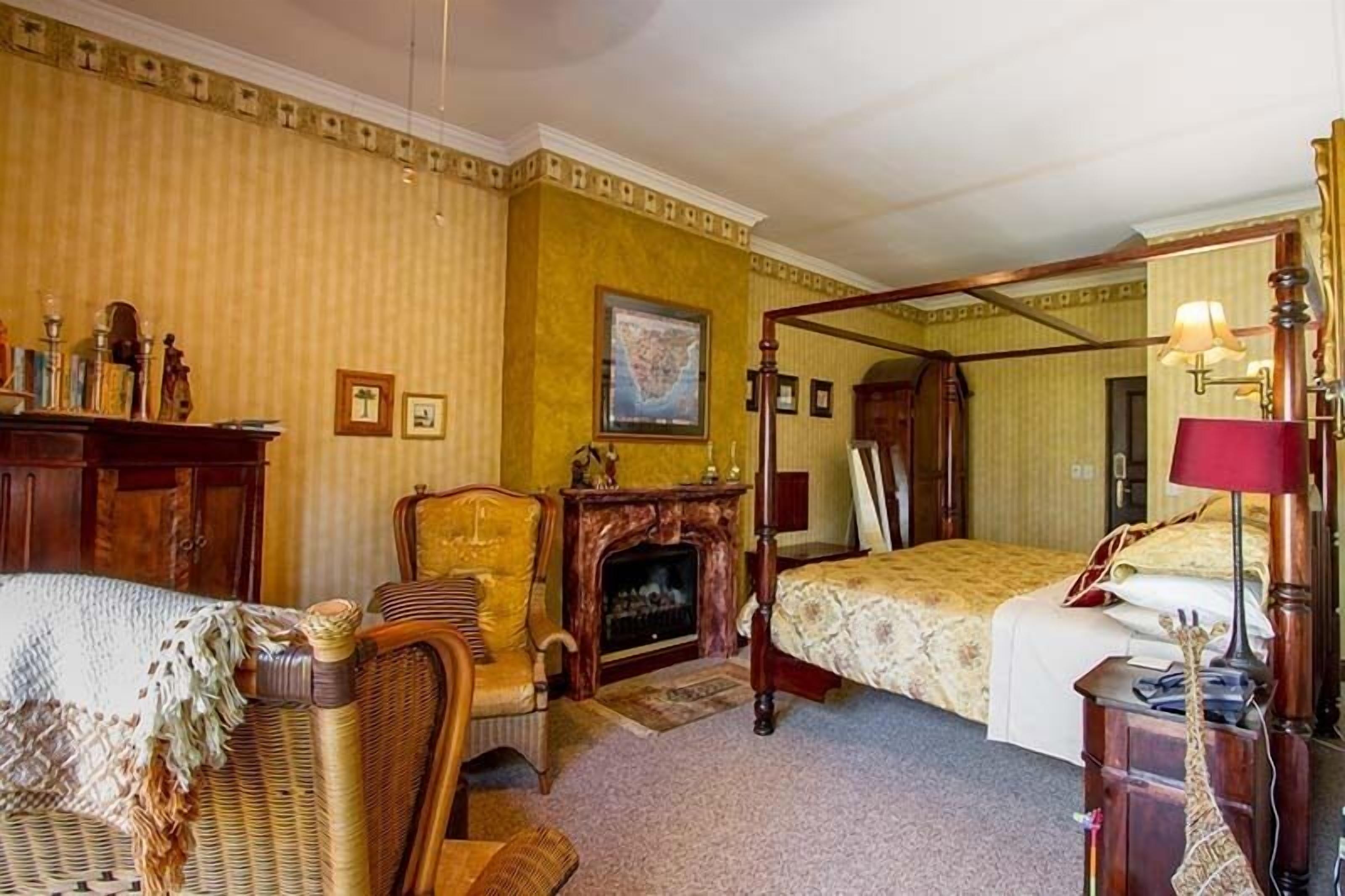 A room with a four-poster bed, a fireplace, a wicker chair, and a wooden desk.