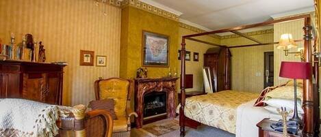 A room with a four-poster bed, a fireplace, a wicker chair, and a wooden desk.