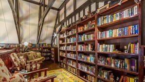 Una biblioteca con scaffali in legno pieni di libri, un tappeto decorato e un divano di legno rivestito di motivi floreali.