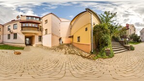 Ein Innenhof mit einem gewundenen Backsteinweg, einem Gebäude mit einem Balkon und einer Treppe, die zu einer weiteren Ebene führt.