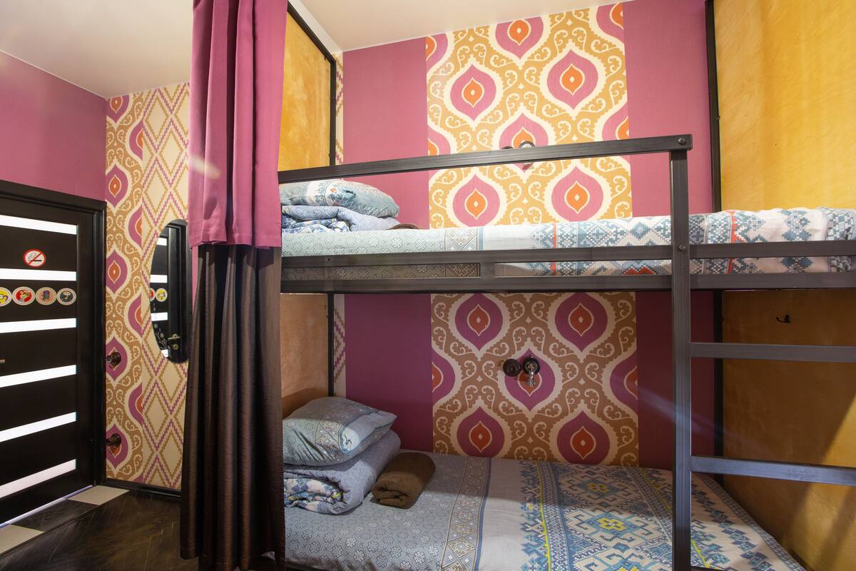 Ein Schlafzimmer mit Etagenbetten, Wandtapete mit Muster, einer Tür mit einem 'Nichtraucher'-Schild und einem Bett mit einer blau-weißen Bettdecke.