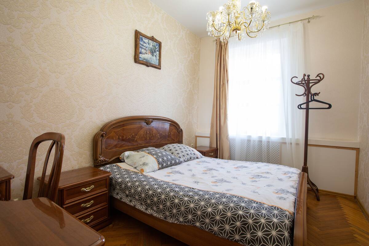 Ein Schlafzimmer mit einem Holzbett, einem Nachttisch, einem Stuhl, einem Kleiderständer und einer Kandelaberleuchte.