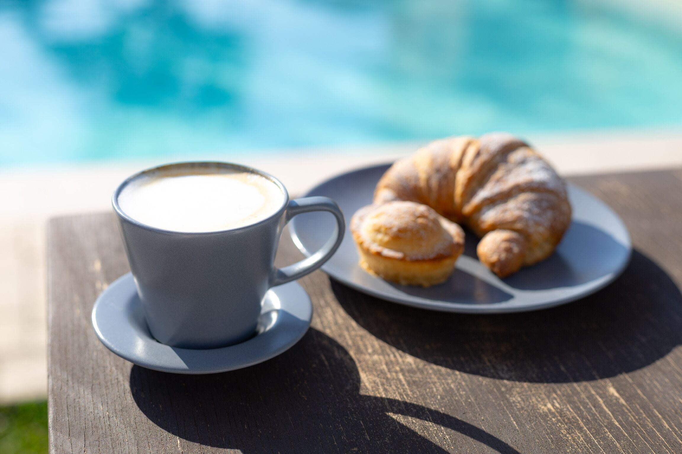 Una tazza di caffè e un croissant su un tavolo vicino a una piscina.