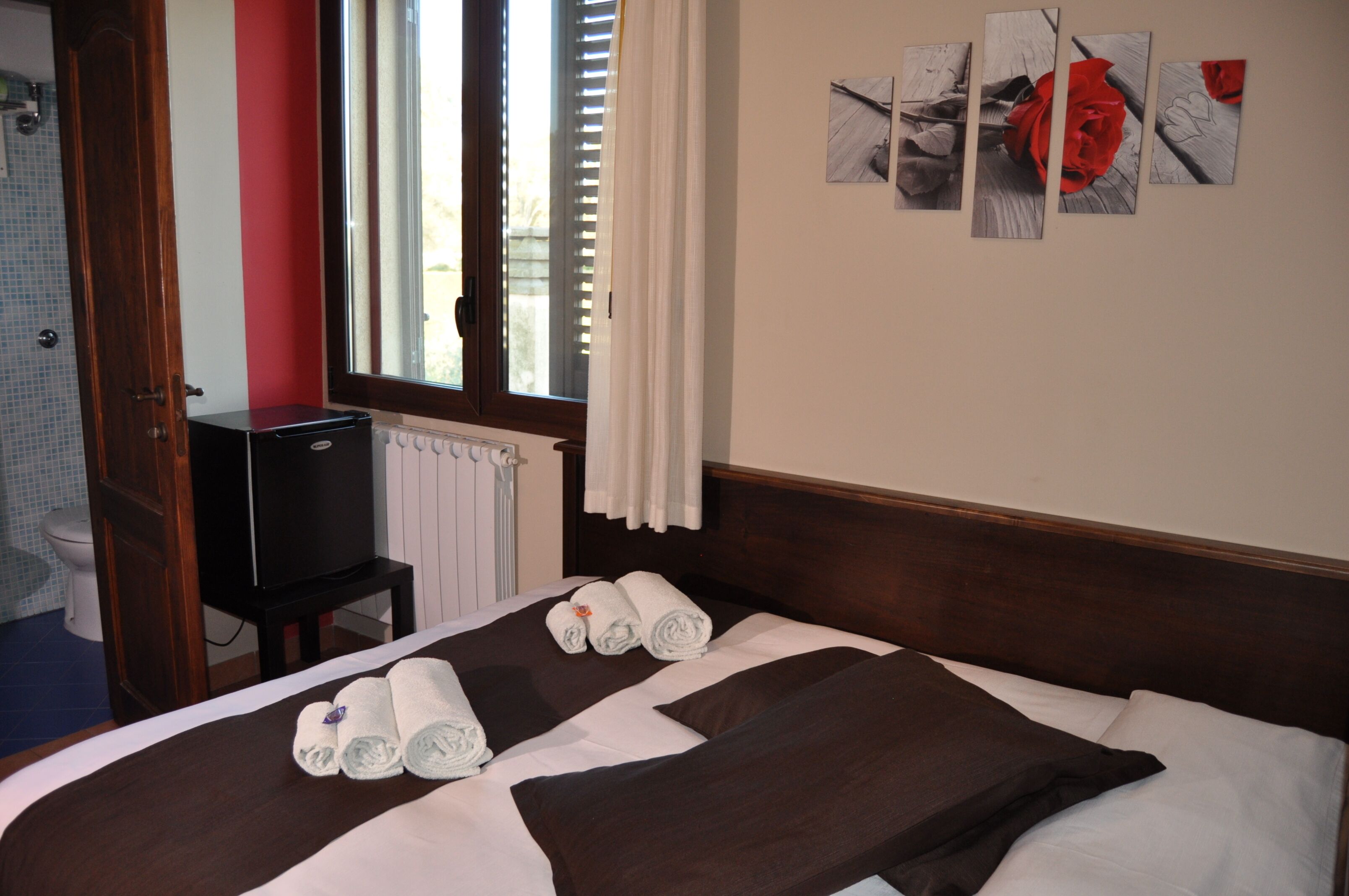 A hotel room with a bed, a TV, a window with curtains, and artwork on the wall.