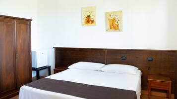 A hotel room with a large bed, wooden headboard, two bedside tables, and a wardrobe.