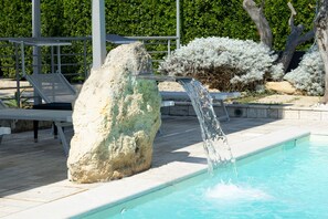 Una piscina con cascada, rodeada de sillas de descanso y una estructura de piedra.