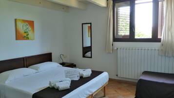 Habitació d'hotel amb llit, una banca, una tauleta de nit, làmpada, quadre, finestra amb cortines i un radiador.