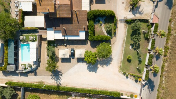 Vista aérea de una propiedad residencial con piscina, un patio cubierto y un camino de entrada.