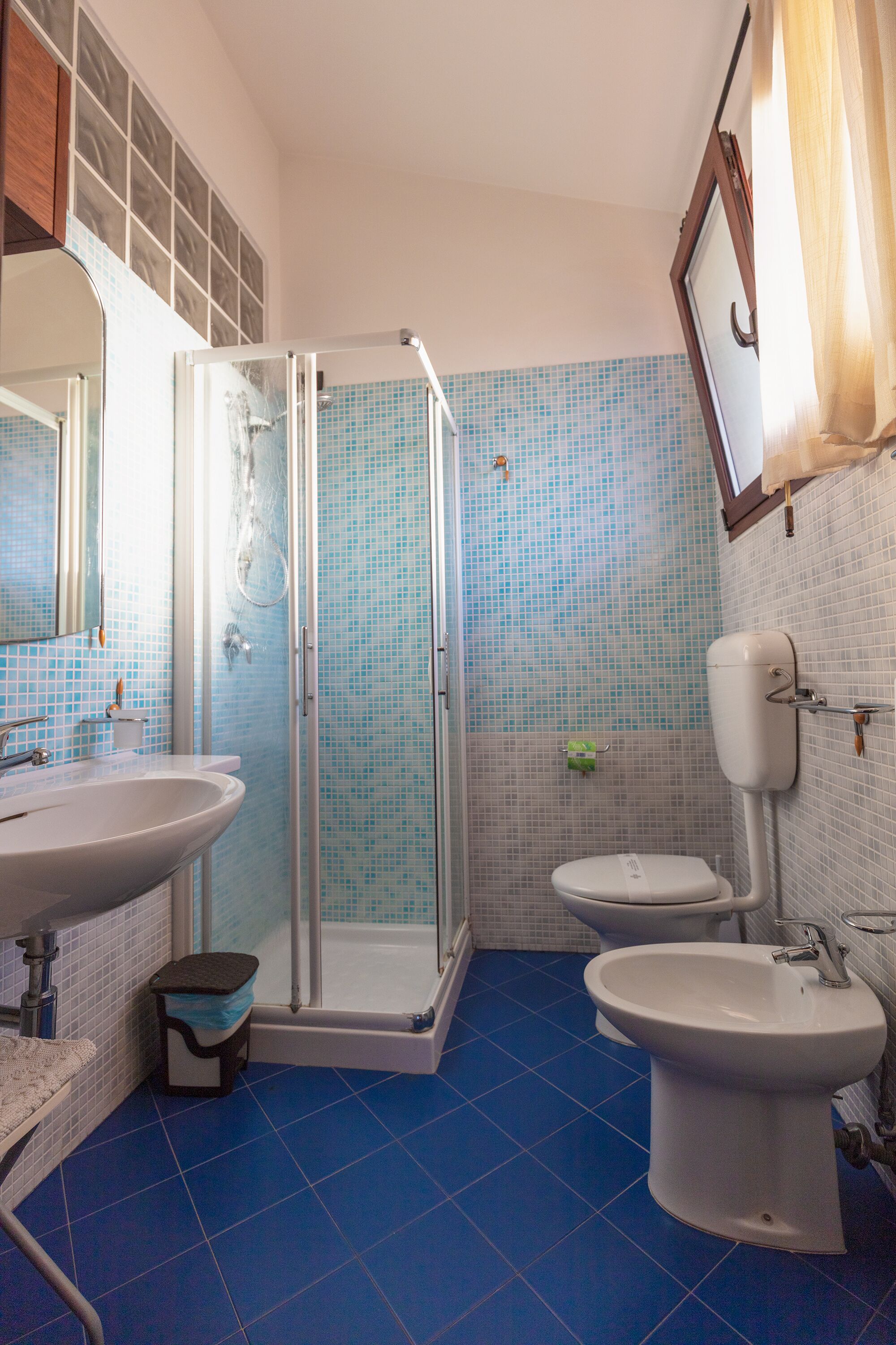 A bathroom with a glass-enclosed shower, a sink, a toilet, and a bidet.