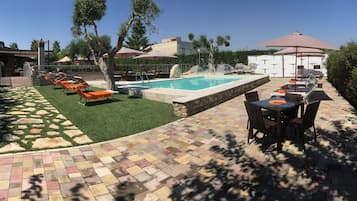 A pool area with lounge chairs, a table, and umbrellas.
