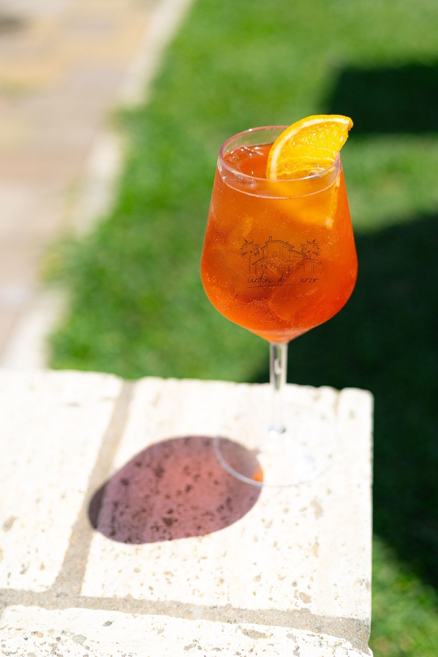 A glass of red beverage with an orange garnish on a white surface.