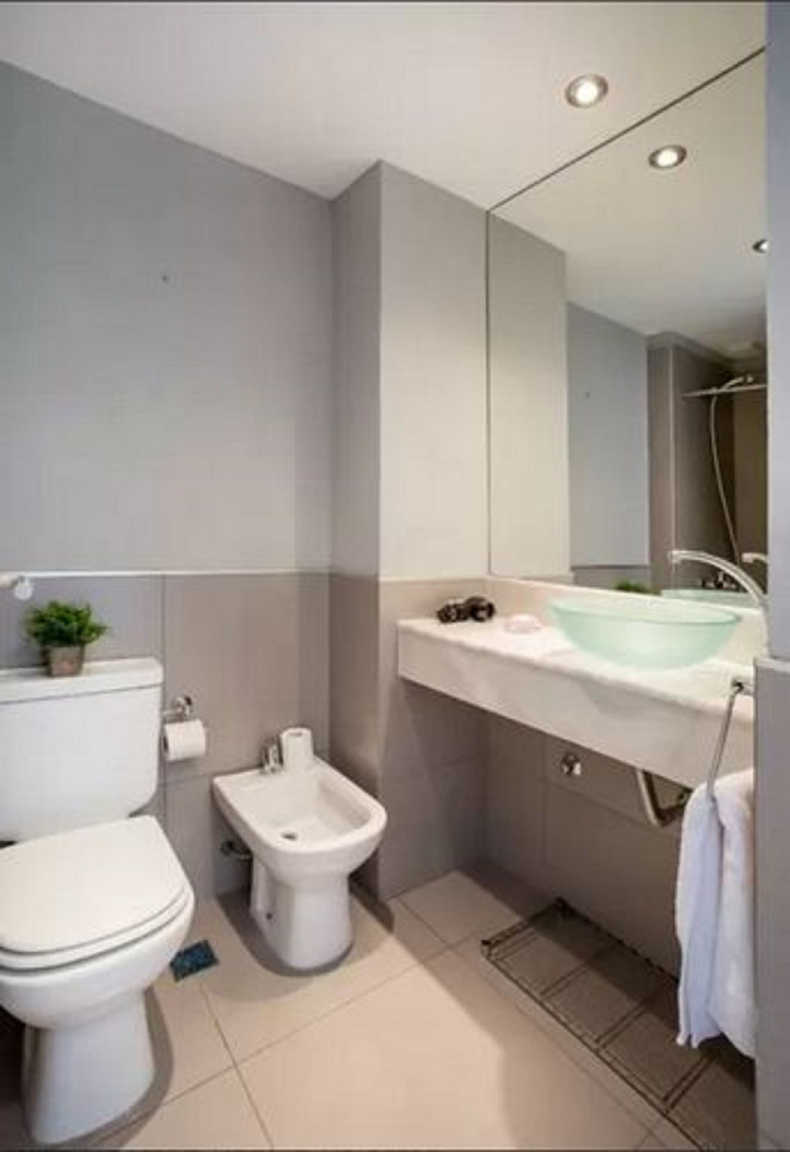 Un bagno moderno con il water, un bidet e un ampio specchio sopra il lavabo.