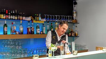 Zona de bar con un bartender preparando bebidas, estantes llenos de botellas de licor y una variedad de vasos.