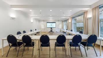 Una sala de conferencias con una larga mesa, sillas, una pantalla de proyector y un amplio ventanal.