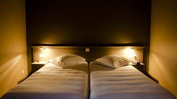 A room with two single beds, each with a nightstand and a wall-mounted lamp.