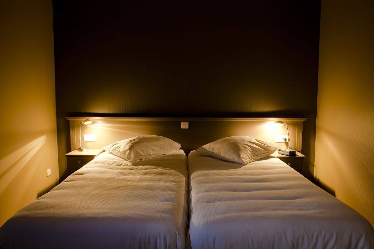 A hotel room with two single beds, each with a bedside table and lamp.