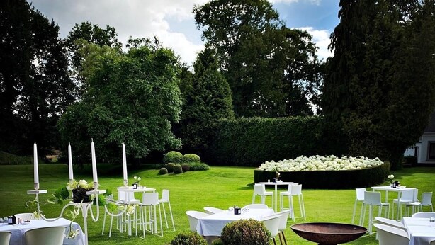 An outdoor wedding setup with tables and chairs arranged on a lawn, surrounded by greenery and a hedge. - Domein Martinus (Zoersel)