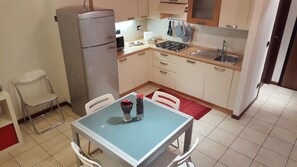 A compact kitchen with a refrigerator, stove, sink, and a dining table with chairs.