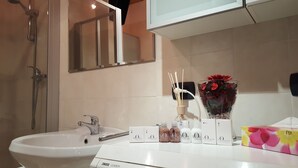Ein Badezimmer mit einem weißen Waschbecken, einem Spiegel, einer Dusche und einer Vase mit Blumen.
