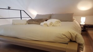 Ein modernes Bett mit Holzrahmen, weißer Bettwäsche und gerollten Handtüchern.