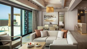 Una habitación de hotel moderna con un sofá grande, zona de comedor y vistas a la playa.