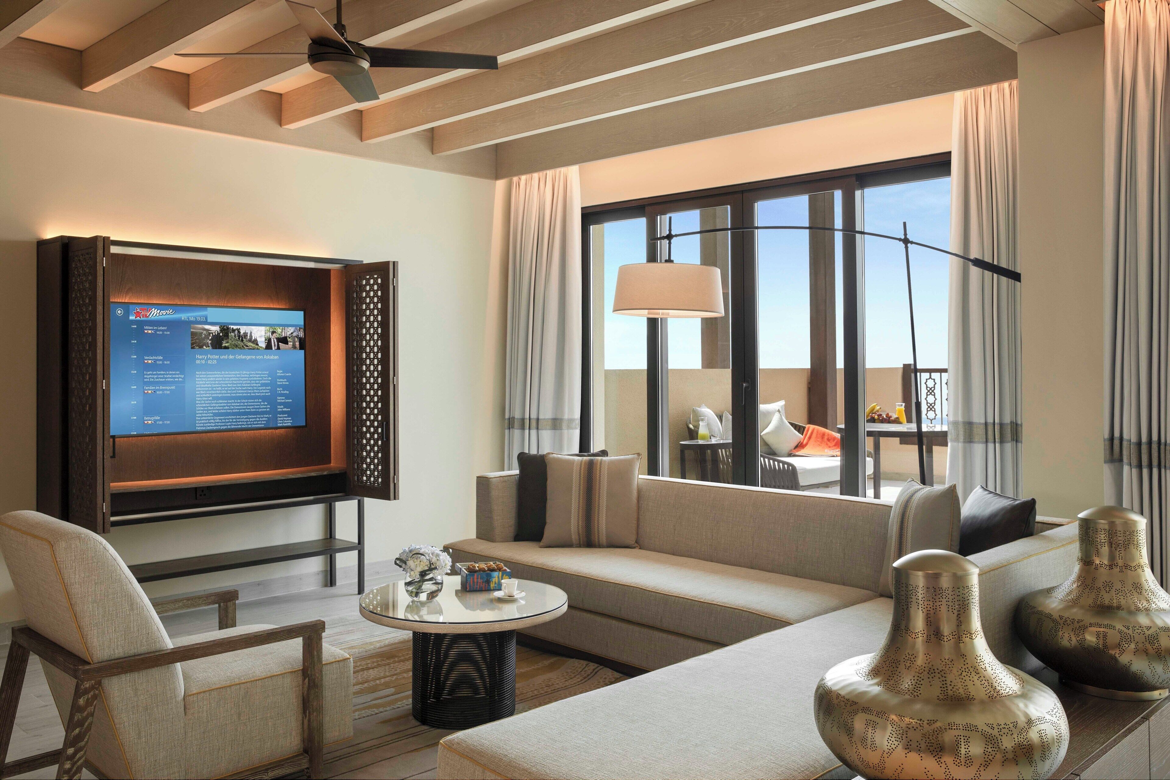 Una sala de estar moderna con televisor de pantalla plana, asientos cómodos, una mesa de centro y un amplio ventanal con cortinas.