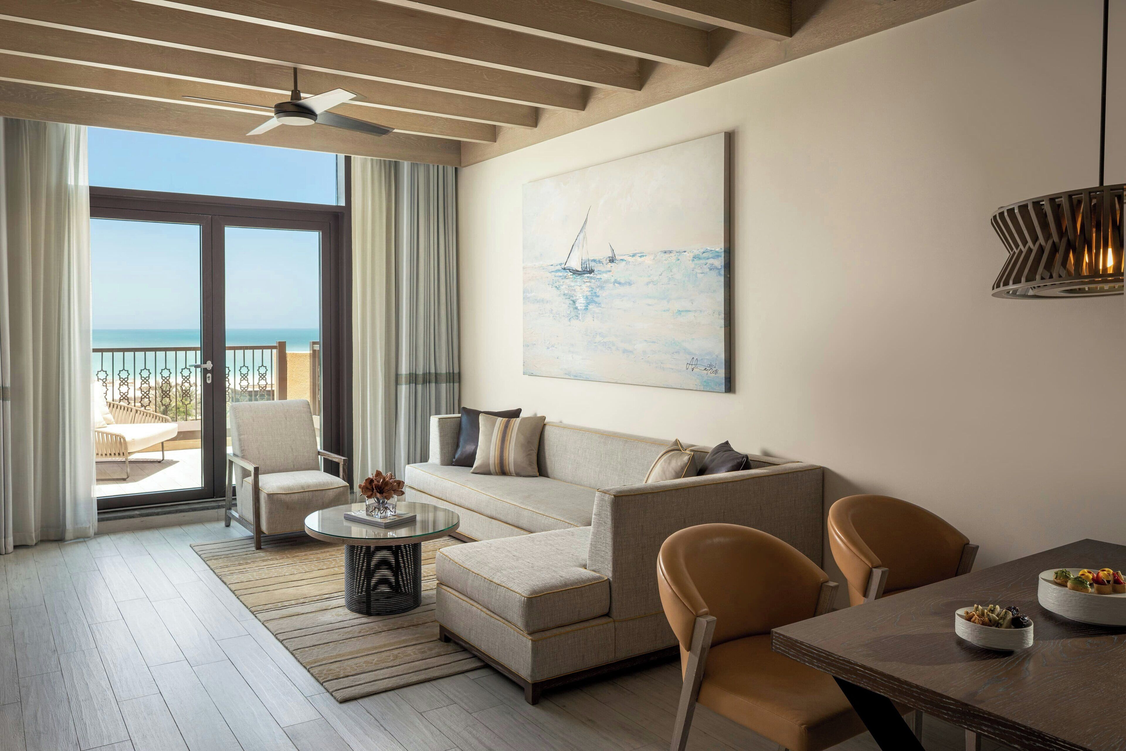 A modern living room with a sofa, chairs, a coffee table, and a painting of a sailboat on the wall.