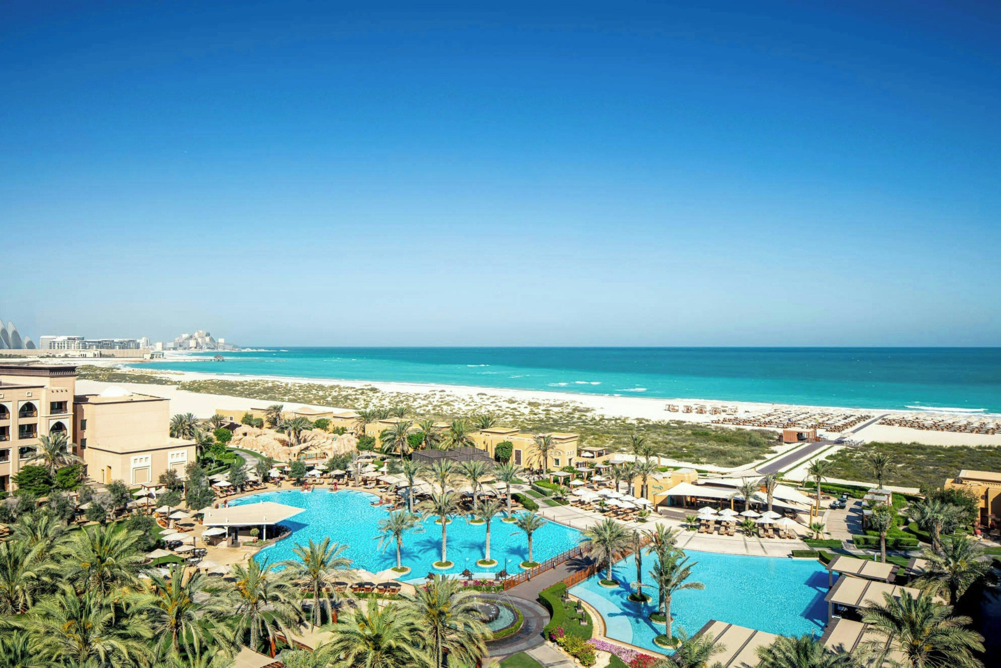 A resort with multiple swimming pools, palm trees, and a beach view.