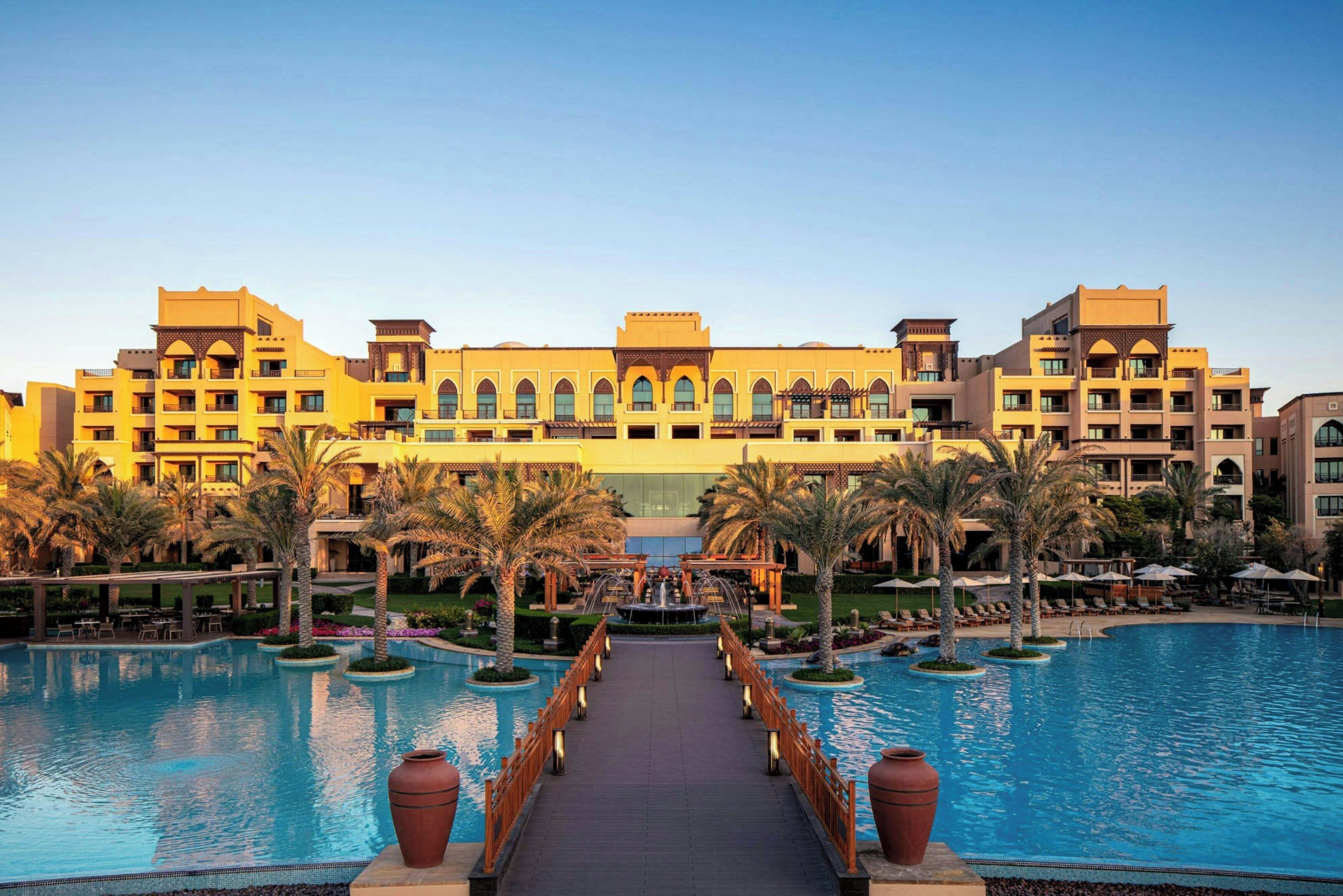 A hotel with a central pool, palm trees, and a bridge leading to the pool.
