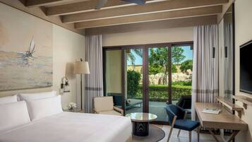 A hotel room with a bed, a desk, a chair, a table, a ceiling fan, a painting, and a view of the outdoors.