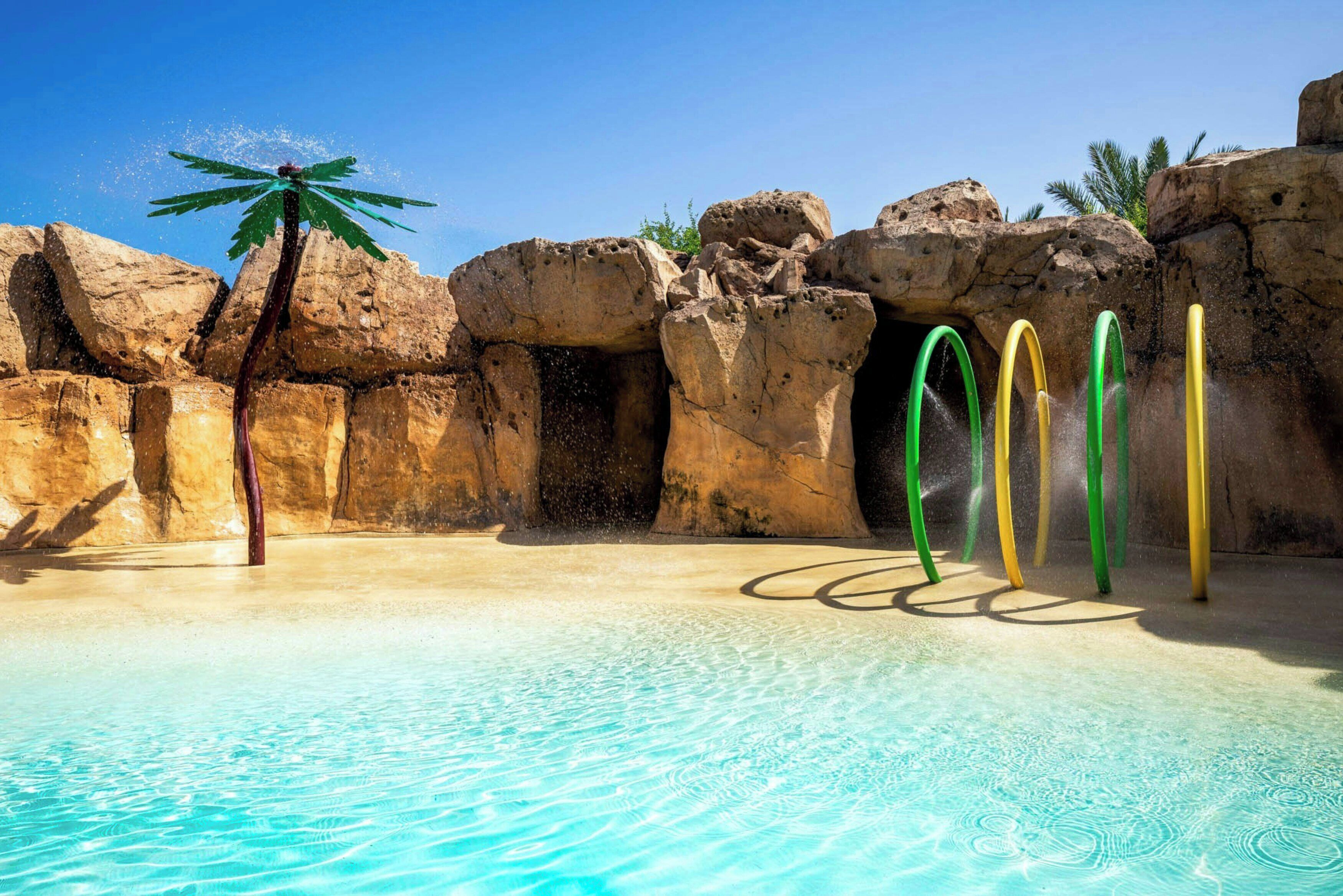 A pool with clear water, surrounded by rock formations and palm trees.