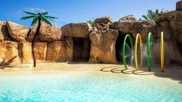 A pool with clear water, surrounded by rock formations and palm trees.