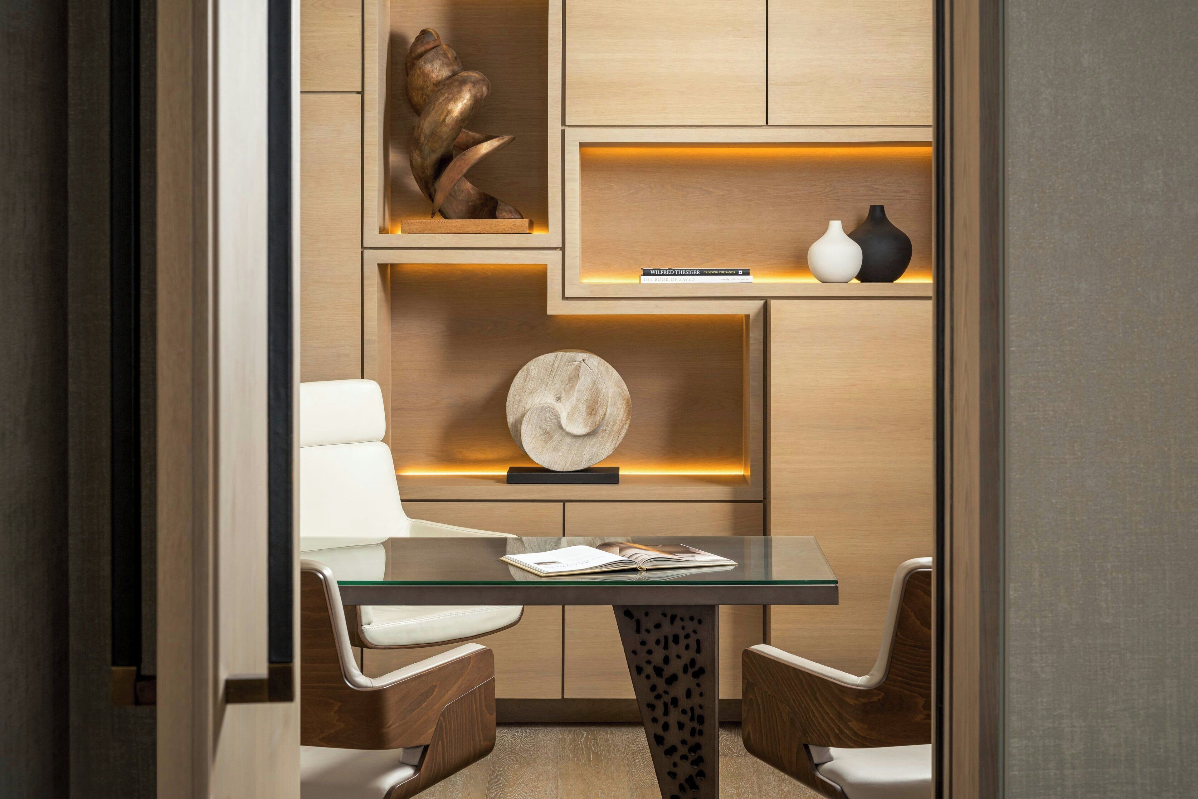 Un interior moderno con una mesa de vidrio, dos sillas, un libro y objetos decorativos en estanterías.