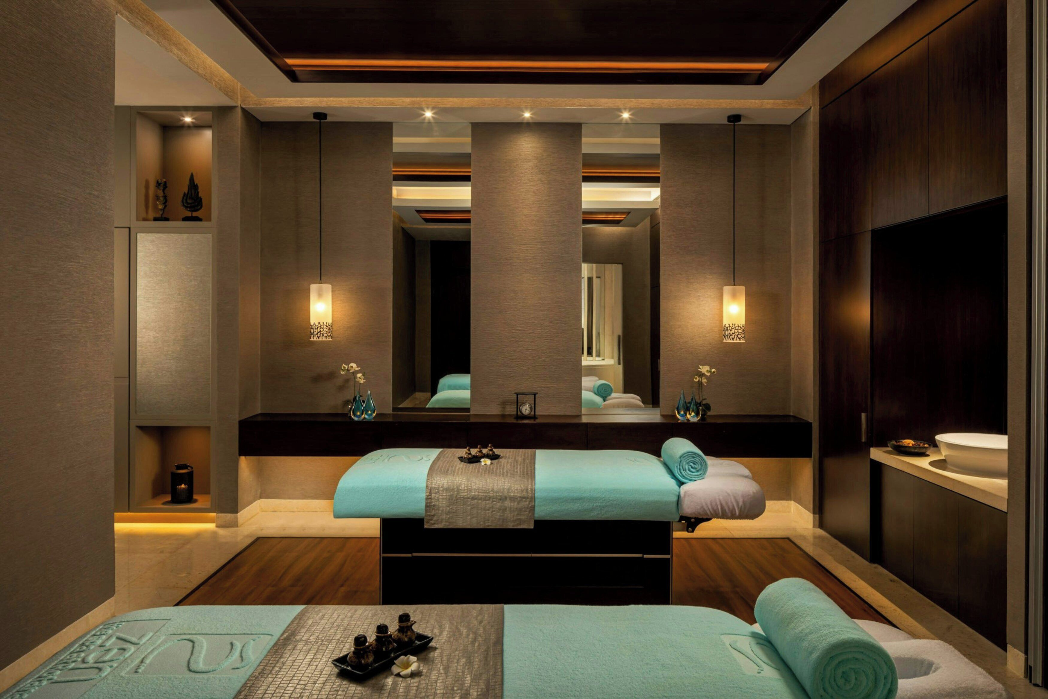 A modern spa room with a large bed, a mirror, and a sink.