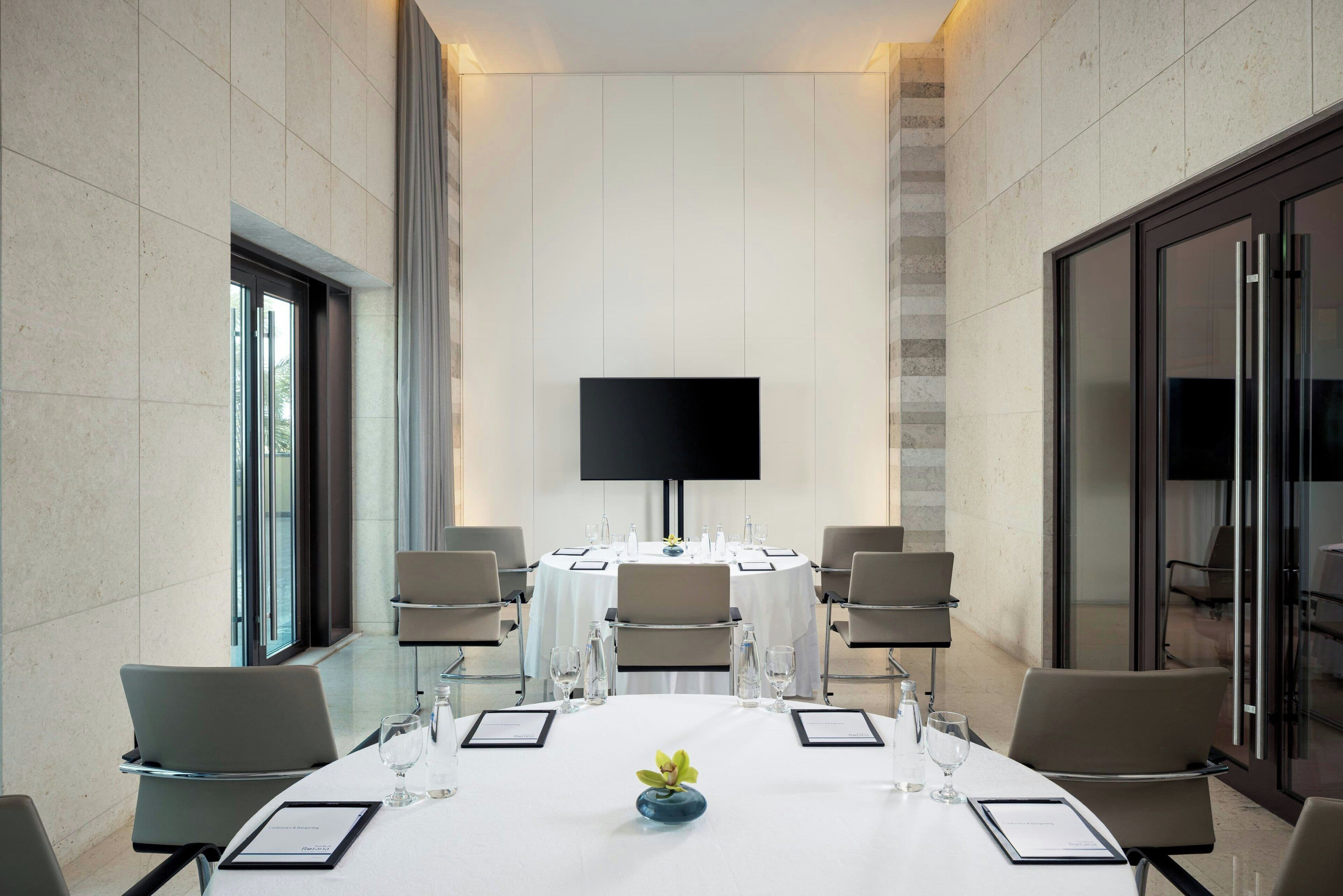 Een vergaderzaal met een groot flatscreen televisietoestel, ronde tafels en stoelen.