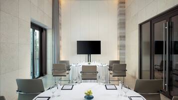 A conference room with a large flat-screen TV, round tables, and chairs.