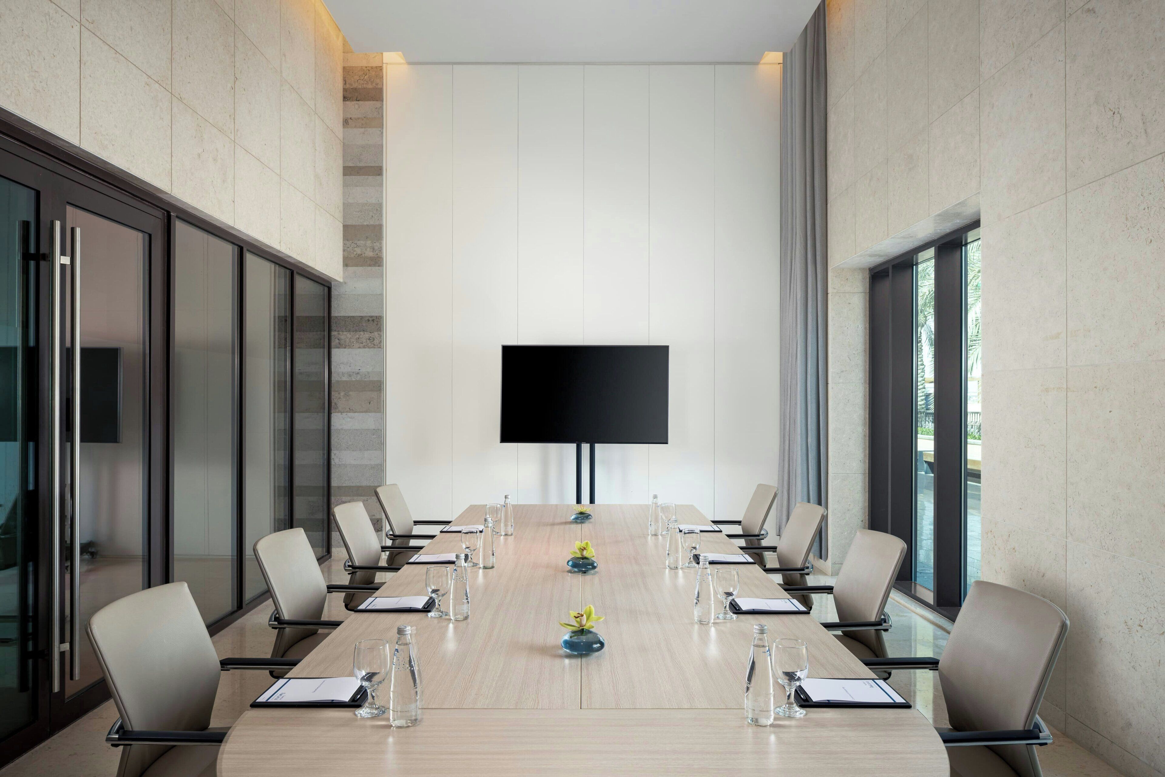 Un salón de conferencias con una larga mesa, sillas, una pantalla de televisión y paredes de vidrio.