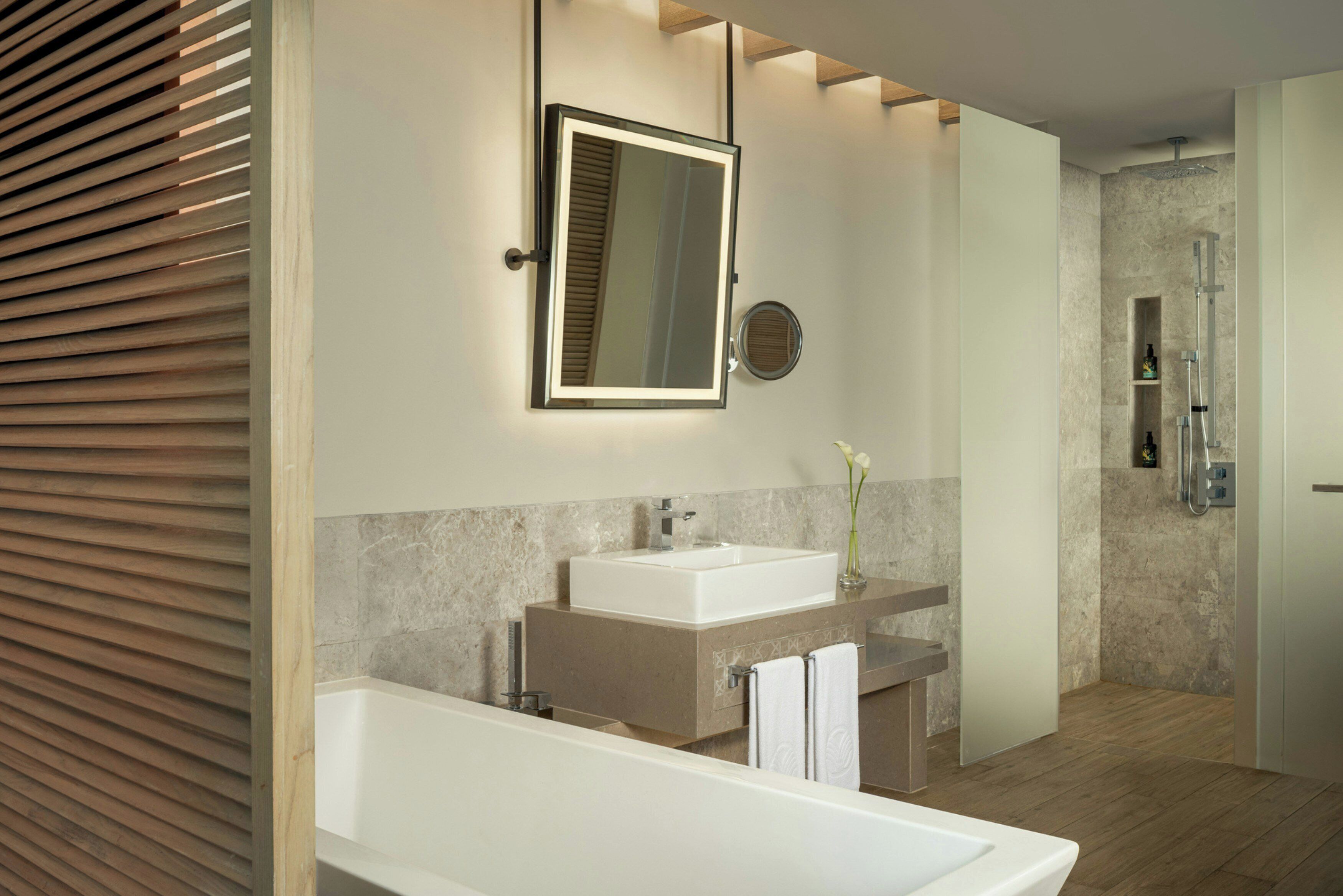 A modern bathroom with a large mirror, a bathtub, a sink, and a shower area.