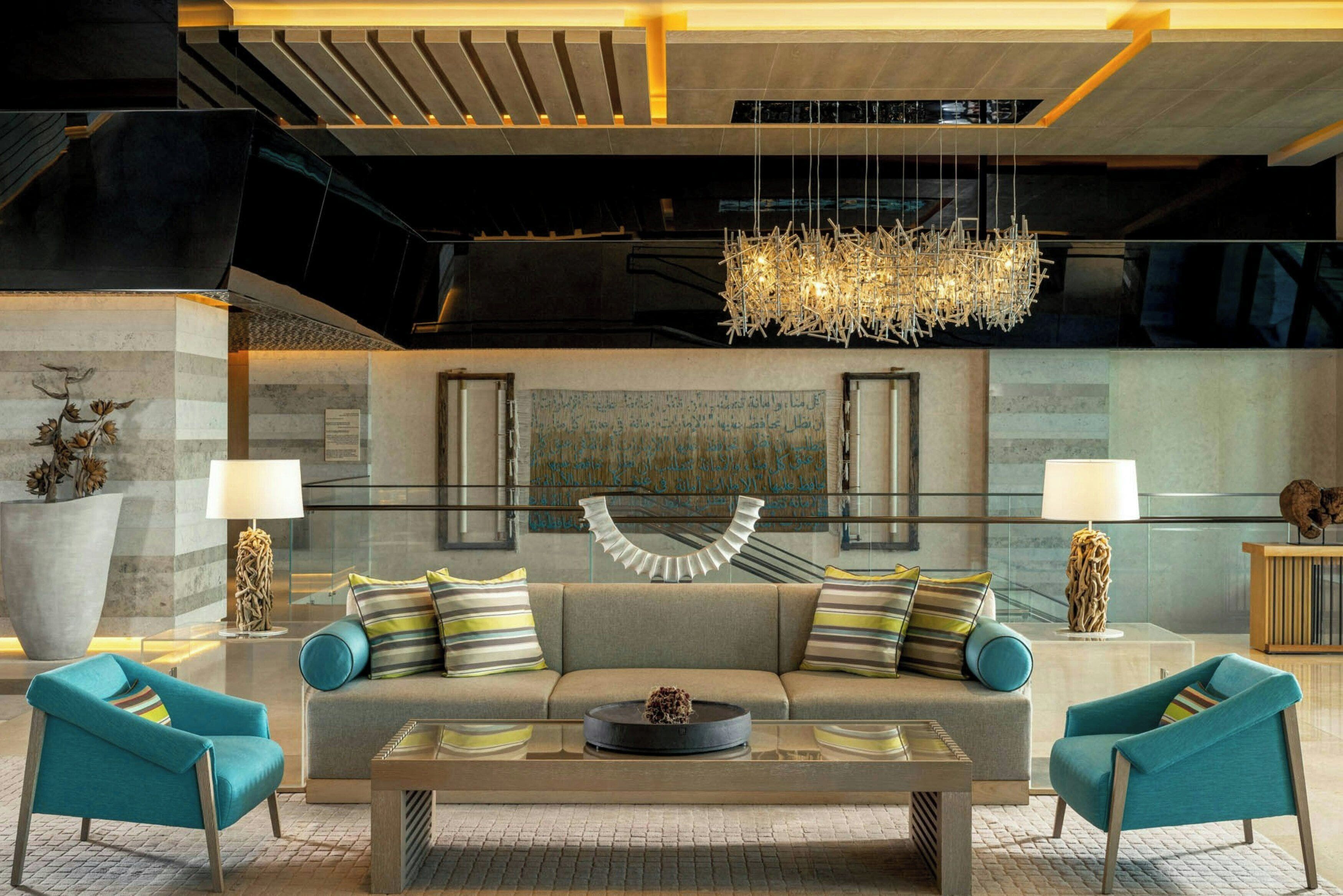 Een moderne lobby met een bank, twee fauteuils, een bijzettafeltje, een kroonluchter en een trap.