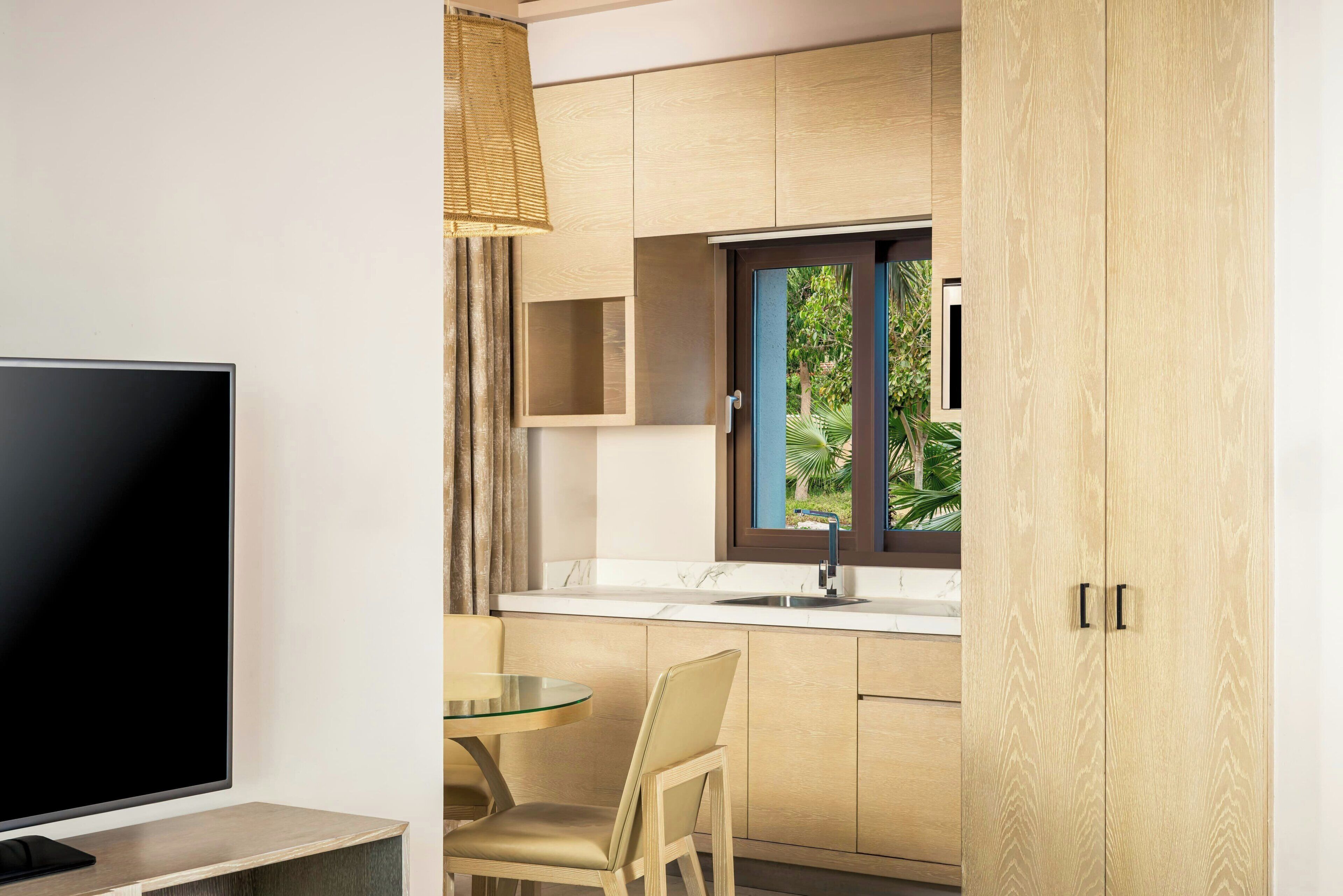 A modern kitchen with a TV, dining area, and a window with a view of greenery.