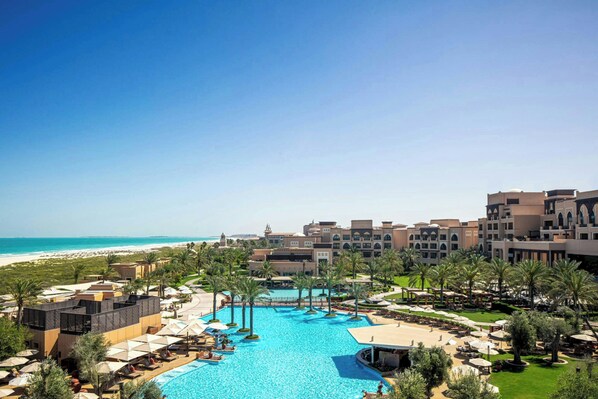 A resort with a large swimming pool, palm trees, and a beach view.